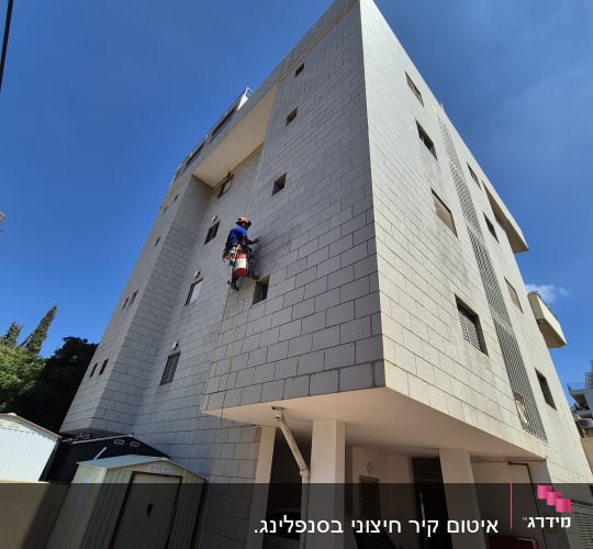 אדם מבצע עבודת איטום על קיר חיצוני של בניין